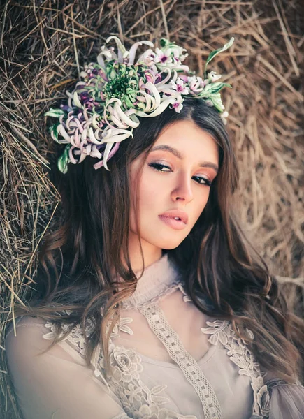 Attractive young woman with beautiful flowers near a haystack. Flowers in the hairstyle, costume jewelry, summer beauty concept. Close-up portrait