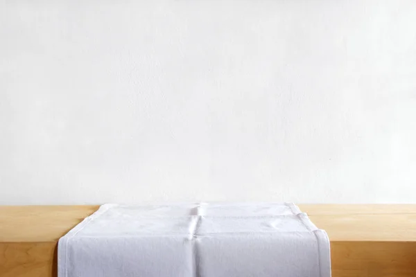 Rustic table with a white table linen against grunge cement wall. Vintage background template, product display montage