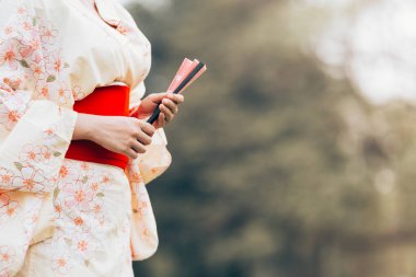 Asyalı kız fan yeşil çimenlerin üzerinde tutan bir kimono stand giyiyor