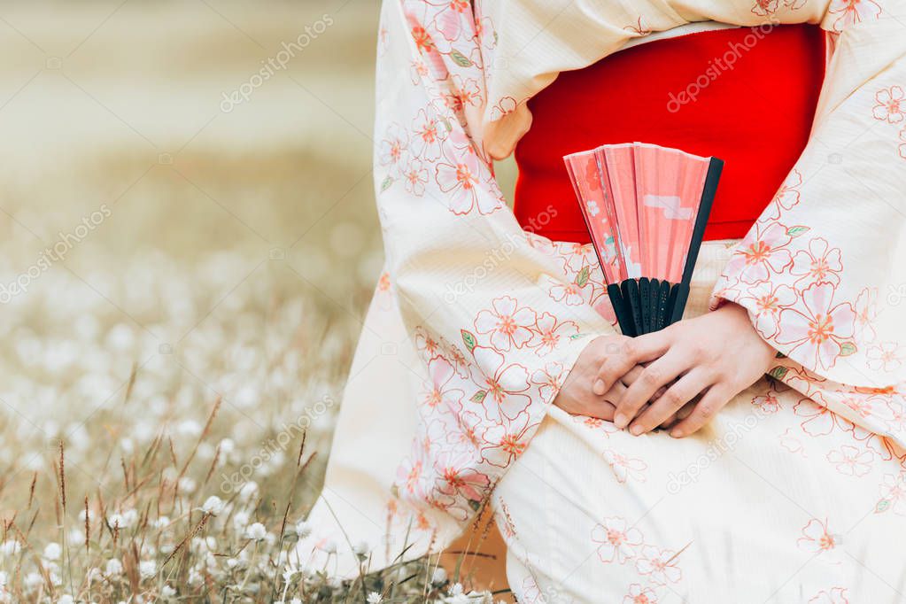 Asian girl wearing a kimono sitting holding fan on a green grass