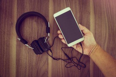 Akıllı telefon ve kulaklık için ahşap arka plan üzerinde müzik dinlemek