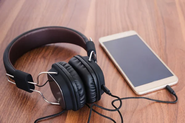 Akıllı telefon ve kulaklık için ahşap arka plan üzerinde müzik dinlemek