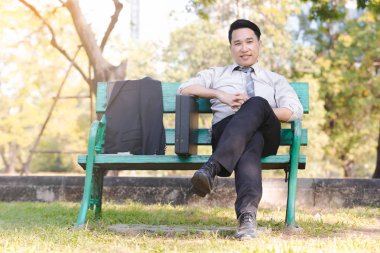 Yeşil ahşap sandalye gevşeme parkta oturmak portre Asya iş adamı