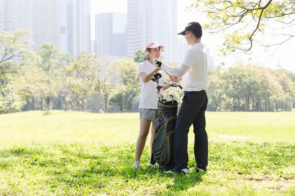 Asian couple playing golf. man teaching woman to play golf while standing on field