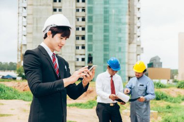 Asya mühendis smartphone iş kavramı ekip çalışması inşaat yapı holding. Proje yüklenici şantiye çalışmalarında planı gözden geçirme.