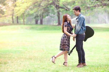 Asya çift çimen parkta oturan akustik şarkı gitar çalmak aşık