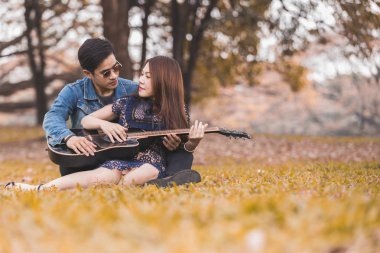 Asya çift çimen parkta oturan akustik şarkı gitar çalmak aşık
