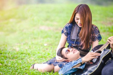 Asya çift çimen parkta oturan akustik şarkı gitar çalmak aşık