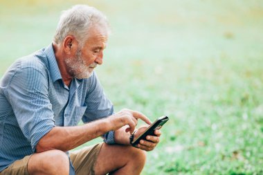 Büyükler düzeyinde men parkta çim üzerinde otururken bir smartphone kullanarak