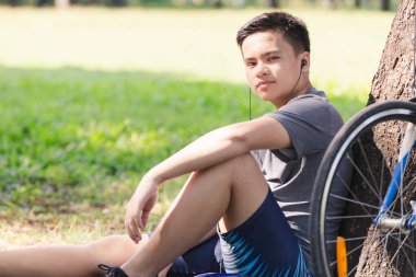 Asya genç adam bisiklet duran ağaç tarafından ve kulaklık ile müzik dinlemek