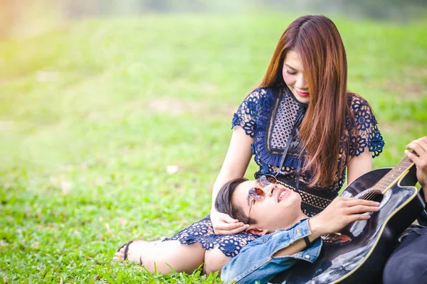 Asya çift çimen parkta oturan akustik şarkı gitar çalmak aşık