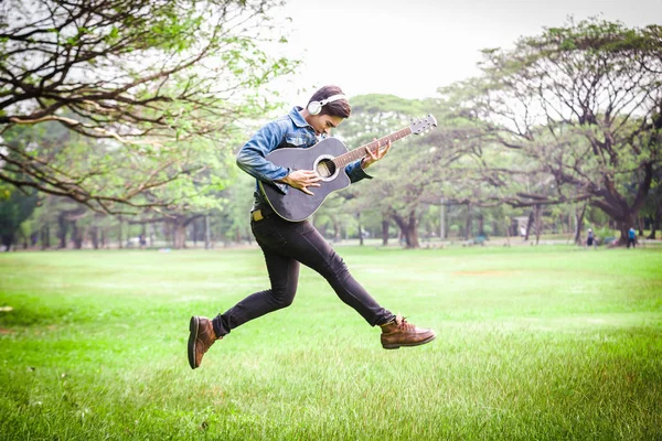 Asian young men jump in nature playing guitar and listen to music with headphones.