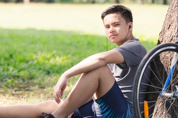 Asya genç adam bisiklet duran ağaç tarafından ve kulaklık ile müzik dinlemek