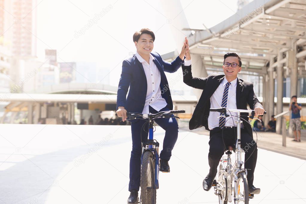 Asian handsome young businessmen talking while riding bicycles in city