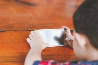 Asyalı küçük çocuk oturan bir akıllı telefon, teknoloji ve insan kavramı ile oyun online oyun