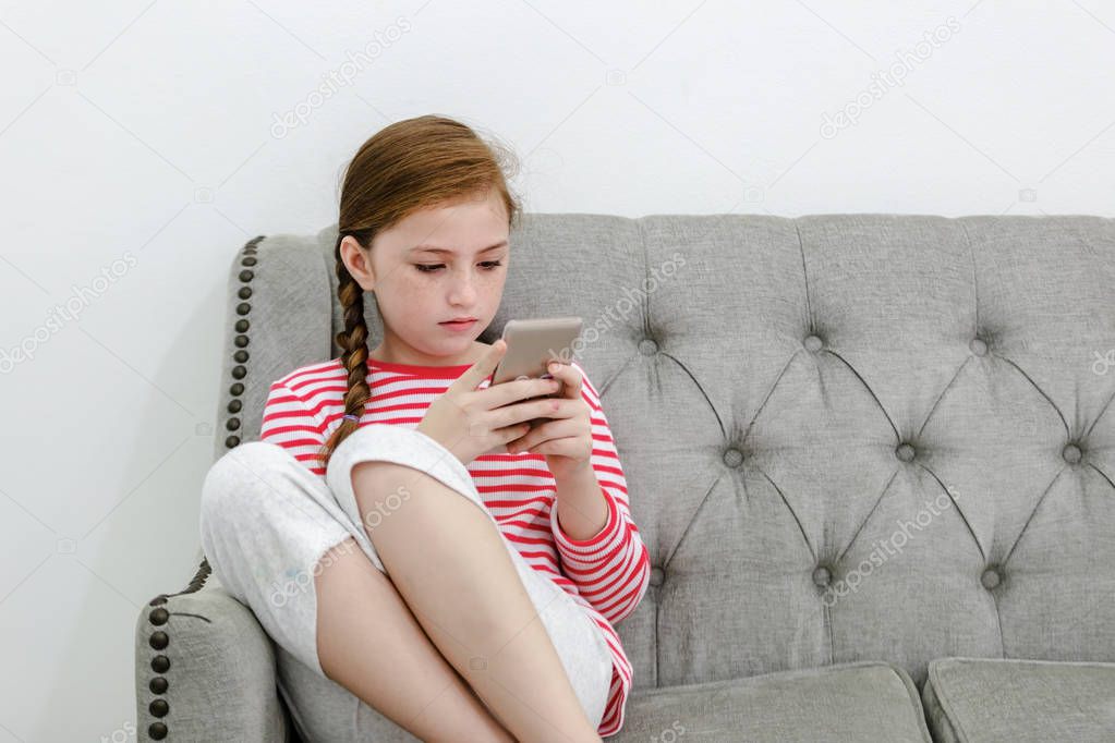Little girl sitting on sofa play smartphone in living room