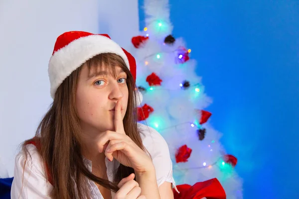 Young woman put her finger to her mouth and ask to be silent near christmas tree