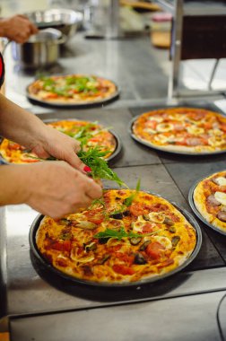 Pizza yapma süreci. Kadın taze roka ile pizzayı süslüyor.