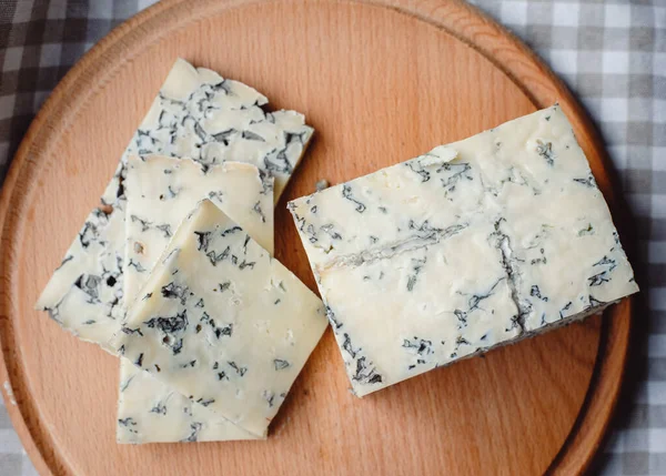 Sliced cheese with blue mold on a wooden cutting board. Cheese composition. Top view. Cheese texture with mold.