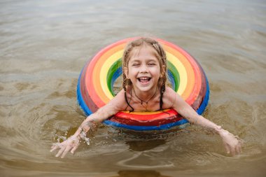 Mutlu kız şişme dairede yüzmeyi öğreniyor. Yaz tatili, sıcak ve su. Çocuk lastik bir çember içinde yüzüyor. Bir çocukla plaj tatili. Suda güvenlik