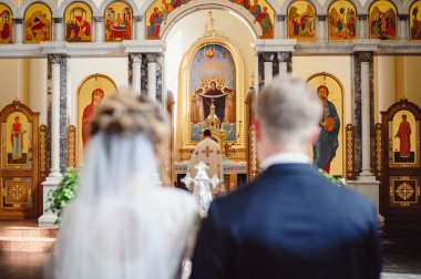 Kilisedeki düğün törenindeki yeni evliler mihraba bakıyor. Rahip gelini ve damadı uzun bir ömür için kutsar. Arka görünüm