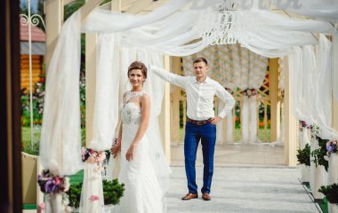 Şık bir gelinlik içindeki güzel, ince gelin, damadın arka planında poz veriyor. Genç çift evlendikleri gün aşık olur.