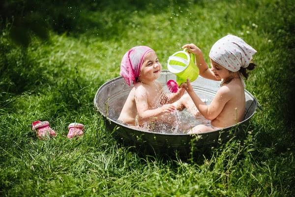 İki kız dışarıda, bahçede banyo yapıyor. Çocuklar kulübede eğleniyor, yuvarlak bir havuzda banyo yapıyorlar. Mutlu çocuk.