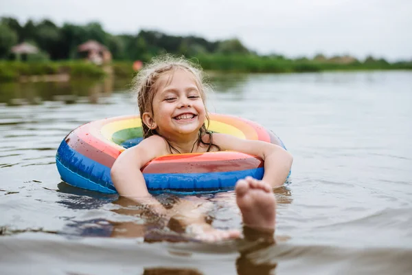 Happy child swims in the river on a colored inflatable circle. Cute little girl gives birth while swimming in the lake. Summer vacation.