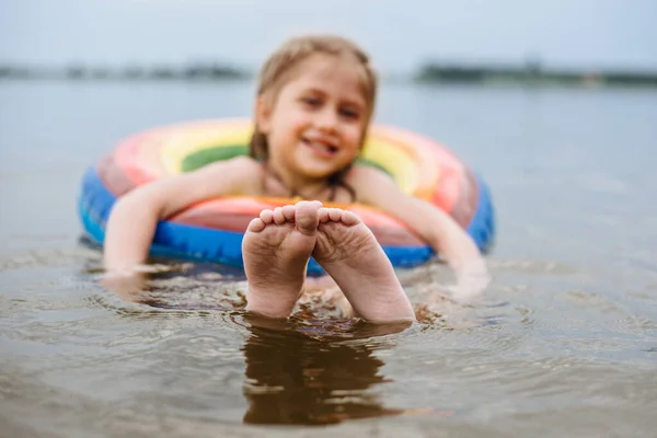 Happy child swims in the river on a colored inflatable circle. Cute little girl gives birth while swimming in the lake. Summer vacation.