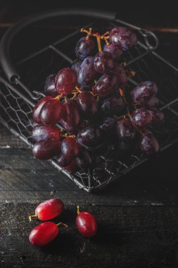 Siyah ahşap zemin, karanlık ruh üzerine metalik sepet içinde kırmızı üzüm.