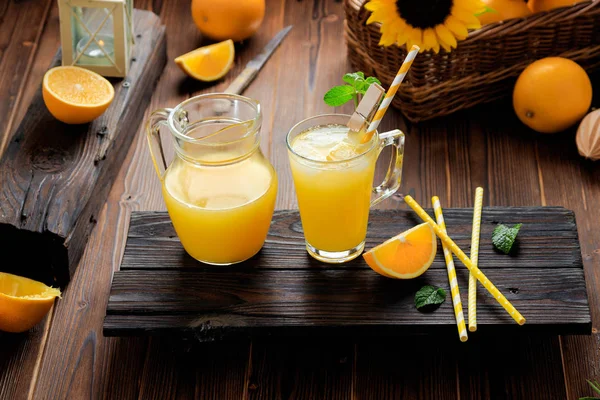 Glass of fresh pressed orange juice with ice cubes and oranges on wooden table. Autumn cozy rustic mood still life — Stock Photo, Image
