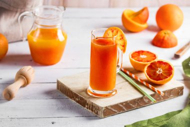 Bir bardak taze sıkılmış portakal suyu ve kan portakal ahşap masa üzerinde. Yaz parlak ruh hali