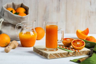 Bir bardak taze sıkılmış portakal suyu ve kan portakal ahşap masa üzerinde. Yaz parlak ruh hali.