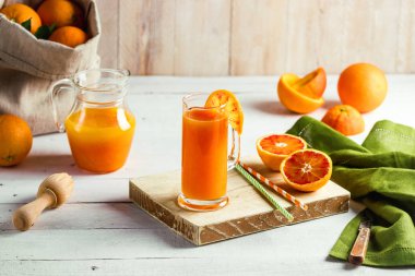 Bir bardak taze sıkılmış portakal suyu ve kan portakal ahşap masa üzerinde. Yaz parlak ruh hali.