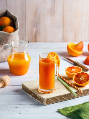 Bir bardak taze sıkılmış portakal suyu ve kan portakal ahşap masa üzerinde. Yaz parlak ruh hali.