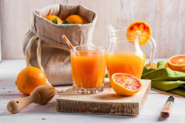 Bir bardak taze sıkılmış portakal suyu ve kan portakal ahşap masa üzerinde. Yaz parlak ruh hali.