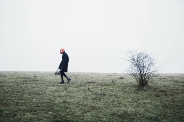 Kırmızı kısa saçlı, siyah elbiseli, dramatik, sisli sonbahar tarlasında genç bir bayan ve kırmızı böğürtlenli çalılık. 