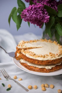 Fındıklı havuçlu kek ve beyaz masa örtüsünde mor leylak buketi, havuçlu bisküvi ve fındıklı ekşi kremayla pişirilmiş turta.