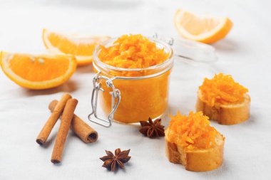 Beyaz masa örtüsü üzerinde iki parça Fransız ekmeği ve beyaz kumaş arka planında ev yapımı reçel olan bir kavanoz turuncu turuncu turşu.