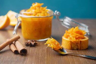 Bir kavanoz portakal, kaşık, Fransız ekmeği, tarçın ve ahşap arka planda yıldız anason, ahşap masada ev yapımı portakal reçeli.