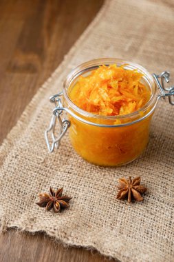 Çuval bezi ve ahşap arka planda yıldız anasonlu bir kavanoz turuncu turuncu turuncu reçel ve çuval ağacının üzerinde birkaç parça ekmek.