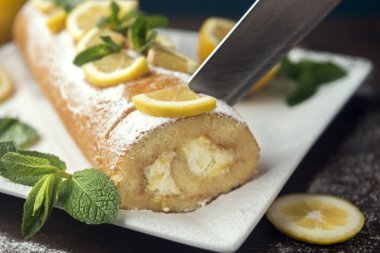 Limon dilimleri ve nane yapraklarıyla süslenmiş limonlu kek, beyaz tabakta tereyağlı kremalı limonlu pasta.