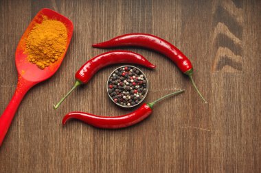 Ahşap bir masada üç kırmızı biber, zerdeçal ve biber meyvesi.