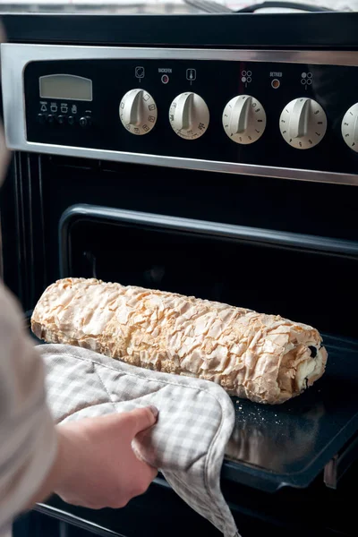 A woman takes out a meringue roll from an electric oven. The process of making meringue roll.