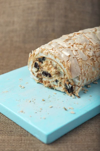 Meringue roll on a white vintage wooden kitchen table with burlap napkin. Meringue pie decorated with prunes and walnuts on blue cutting board.