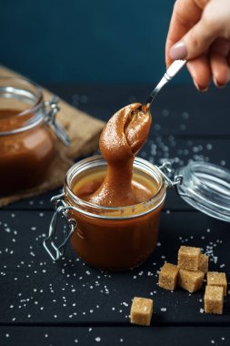 Cam kavanoz ev yapımı tuzlu karamel ve siyah ahşap bir masada kaşık. 