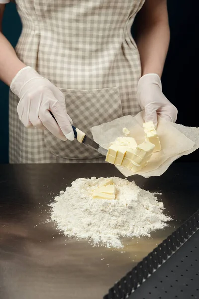 Cook placing small pieces of butter into flour on kitchen table from stainless steel. Safely cooking process of tart, cookies or bakery. Gloved hands.