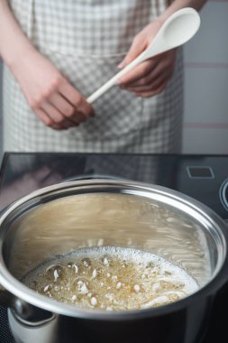 Ahşap kaşıklı karamelli önlüklü kadınlar paslanmaz çelik tavada karamel hazırlıyorlar.