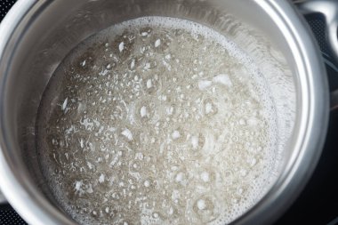 Paslanmaz çelik bir tavada kaynatılmış şeker pekmezi. Metal bir kapta şeffaf sıvı kaynıyor.