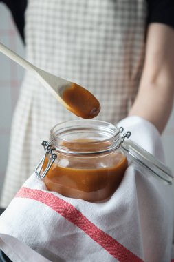 Kareli önlüklü bir kadın cam kavanozda taze karamel tutuyor. 